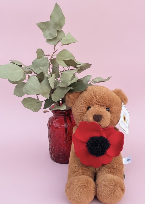 Poppy Bear with Eucalyptus - A soft brown teddy bear clutching a single large red plush poppy makes an irresistibly playful gift for a birthday, just because, or a sweet romantic surprise. The bright red fabric flower pops against the bear's warm fur and pale pink backdrop, creating an immediate sense of affection and whimsy that feels handcrafted and personal-perfect for saying "I'm thinking of you," "congratulations," or "thank you."  The set arrives styled in a red glass vase filled with fragrant eucalyptus stems, adding fresh green texture and subtle scent to the presentation. Dimensions are compact and gift-ready: a plush bear paired with one oversized fabric flower and a vase that fits easily on a desk or bedside table. Ideal for Father's Day, Valentine's Day, Mother's Day, graduation, housewarming, or to brighten someone's day-this cheerful bundle needs very little care beyond occasional fluffing of the bear and keeping the eucalyptus away from direct heat. Order for same-week giving to ensure your person feels genuinely seen and celebrated.
