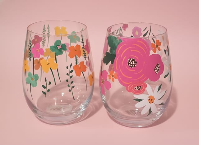 stemless floral w/ calendiva plant - A compact burst of spring warmth, this stemless floral arrangement pairs a cheerful pink-flowering plant with two hand‑illustrated stemless glass tumblers - a perfect combo for a housewarming, birthday, new baby, or just-because surprise. The arrangement reads as a bright, casual gift that says "thinking of you" or "thank you" without fuss; the rounded clusters of blooms and glossy green leaves give a fresh, uplifting presence that will make the recipient feel genuinely seen.  The plant's neat, compact habit features small pink blooms rising above thick, glossy green foliage, planted in a clean white textured ceramic pot that fits easily on a windowsill or bedside table. The two clear stemless tumblers bring playful pastel charm: one patterned with scattered tiny flowers in pink, yellow, orange and teal, the other centered on a larger pink bloom with delicate accents. Together they create a coordinated gift set in soft pinks, peaches, yellows and greens that reads as thoughtful and versatile.  Ideal for spring and lovely year‑round, this set works beautifully as a thank-you, anniversary, Mother's Day, or newborn welcome gift - the plant offers lasting color while the tumblers are ready for everyday use. The compact size makes care simple: bright, indirect light and regular watering keep the foliage glossy and blooms returning, and the ceramic pot provides a tidy, gift-ready presentation for immediate display.