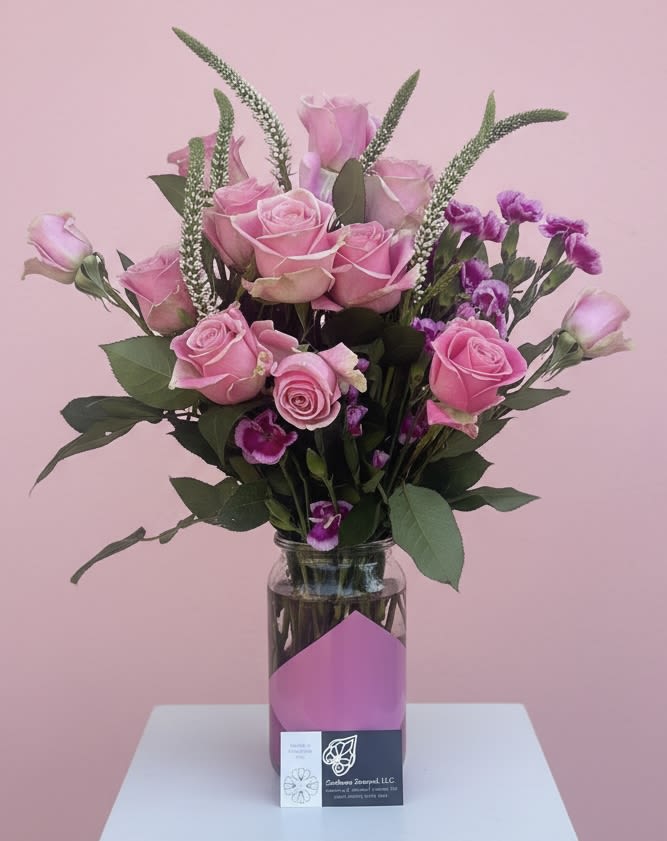 Veronica and Roses  - A cluster of pink roses with airy, white-speckled veronica spikes creates a romantic, celebratory statement perfect for an anniversary bouquet or a birthday surprise. This flower arrangement places the recipient at the center-she'll feel noticed and cherished when soft pink roses meet delicate purple filler blooms and tall, graceful veronica for height. It also reads beautifully for love and romance, thinking-of-you moments, or a just-because pick-me-up.  Crafted in a clear glass vase with a paper-wrapped base and a business card tucked in, the upright composition pairs broad dark foliage with pastel petals for contrast and texture. In addition to roses, gentle carnations and small purple accents fill out the design in green, pink, purple, and white tones; the visible vase gives it a finished, florist-made look that fits well for housewarming, new baby celebrations, graduations, or as a tasteful sympathy or get-well gift.  Light-care instructions: keep the vase filled with fresh water and trim stems every few days to prolong bloom life. Available in a single size as shown-an elegant option to say thank you, congratulations, I'm sorry, or to honor Mother's Day, Valentine's Day, Women's Day, or summer festivities with a thoughtful, timeless arrangement.