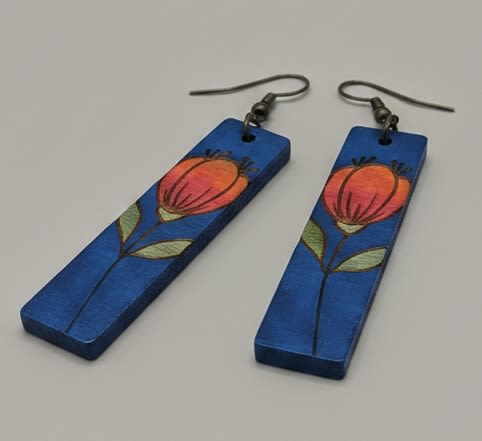 Wooden Tulip earrings - Bright, hand-painted wooden tulip earrings that read like a pocket-sized bouquet-perfect as a thoughtful birthday or "just because" gift for someone who loves color. These long rectangular earrings feature a deep blue background showcasing a single orange-pink tulip with small green leaves outlined in dark, graphic lines; the artisanal, painterly contrast gives them a joyful, modern look ideal for spring, thinking-of-you, or love-and-romance moments.  Lightweight and wearable, each earring hangs from simple metal hooks so they move like a little flourish when worn. The bold color story-pink, blue, green, and orange-pairs easily with casual and dressy outfits and makes them a sweet choice for Mother's Day, Women's Day, Valentine's Day, Easter, or a thank-you surprise. Treat someone to a small, wearable bloom that says you noticed them; these arrive ready to gift and require no care beyond the occasional gentle wipe.