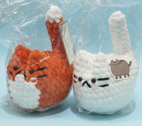 Crochet Kitty -locally made! in white or orange and white - Handmade charm and small-town warmth come in the form of a crocheted cat plush-perfect as a sweet add-on gift for Father's Day, a birthday, or a "just because" surprise. These soft, textured kitty toys (choose orange-and-white or all white with black facial details) arrive packaged in a clear plastic bag with a hang tag, giving the person you're thinking of a delightfully homespun token that feels personal and playful.  Each kitty is crocheted from soft yarn with upright tails, stitched facial features, and small details like pink cheeks on the white version, making them tactile and endearing. The package includes the plush tucked into a protective plastic bag and finished with a printed hang tag, sized to work as a stocking stuffer, desk companion, or bedside keepsake. Ideal as a companion to a bouquet, a thoughtful get-well pick-me-up, or a tiny retirement, anniversary, or holiday treat-these kitties suit Christmas, Mother's Day, Admin Professionals' Week, Best Friends Day, and other moments when you want to make someone feel seen.
