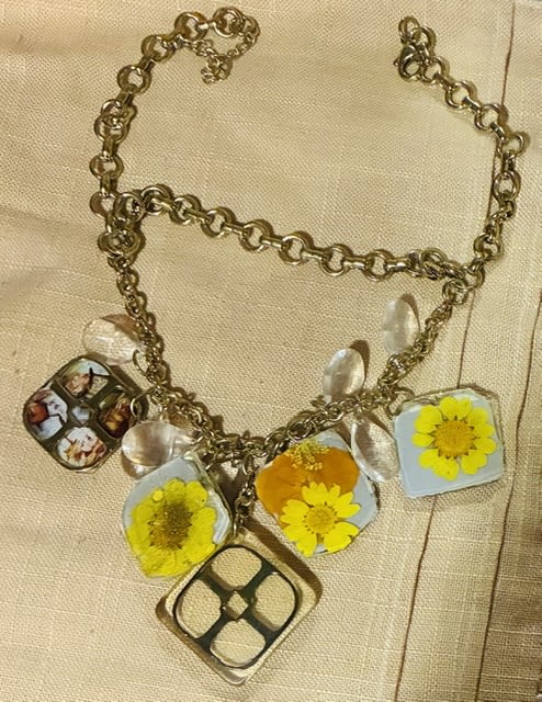 Resin and Daisy Alice in wonderland themed charm necklace  - Bright, nostalgic daisies pressed in clear resin give this charm necklace a sunny, giftable feeling-perfect as a birthday keepsake or a casual "thinking of you" gift. As a floral accessory for someone who loves vintage whimsy or Alice in Wonderland-inspired trinkets, it reads like a tiny bouquet they can wear: cheerful yellow petals and crisp white accents suspended along a delicate metal chain.  Handmade square resin pendants hold real pressed daisy blooms and a single miniature collage image, each set in metal square settings that catch the light and invite close-up admiration. The warm yellow and white palette pairs easily with everyday outfits; the pieces are lightweight and arranged along a simple chain for layered charm without feeling fussy.  Give this to the friend who treasures sentimental keepsakes, a sister celebrating a small milestone, or anyone who appreciates floral jewelry that feels personal. Care is simple-avoid prolonged water exposure and store flat to keep the pressed flowers bright; the necklace ships ready to gift.