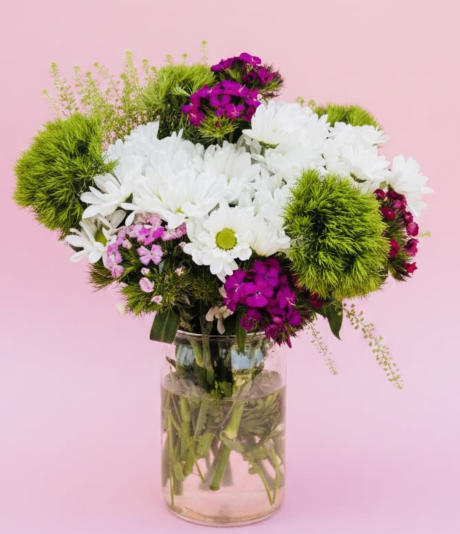 White Daisy Bouquet  - A dense cloud of white daisy-like blooms meets pops of magenta and purple in this fresh bouquet-perfect as a birthday bouquet or a cheerful everyday gift. The arrangement reads playful and garden-fresh, so the person you're thinking of will feel noticed and brightened the moment they see the crisp whites contrasted with energetic pinks and purples.  This full, rounded arrangement pairs white daisies with vivid magenta and purple filler flowers and bright green mossy pom-pom accents (green dragon/mum balls) for added texture and whimsy. Stems are gathered in a clear glass vase that displays the natural, water-filled stems below, giving a clean, modern look. Ideal for spring celebrations, get-well wishes, or just because moments-no special care beyond fresh water and a cool spot; replace water every few days to keep blooms looking their best.