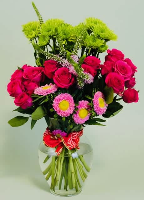Pink roses and mixed daisies in a clear glass vase with a red ribbon