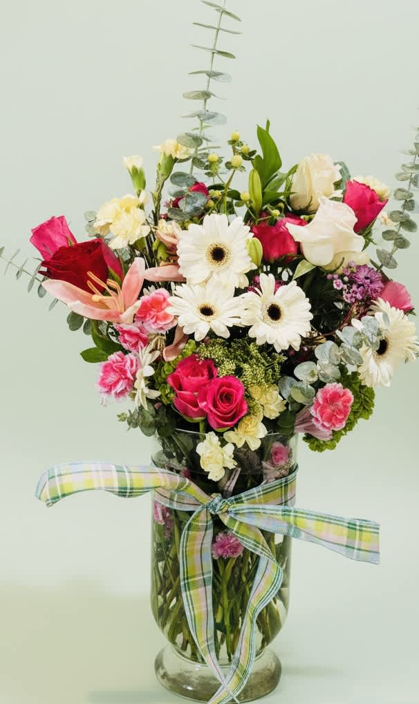 Mixed bouquet of pink and white flowers in a glass vase with a plaid ribbon