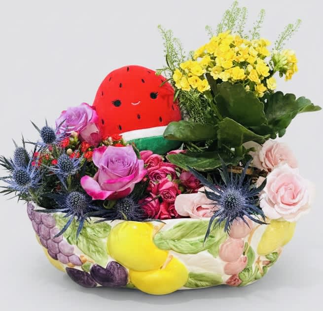 Mixed flower arrangement with a watermelon plush centerpiece in a painted ceramic container