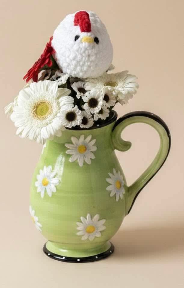 Daisy arrangement in a green pitcher with a crocheted chicken topper
