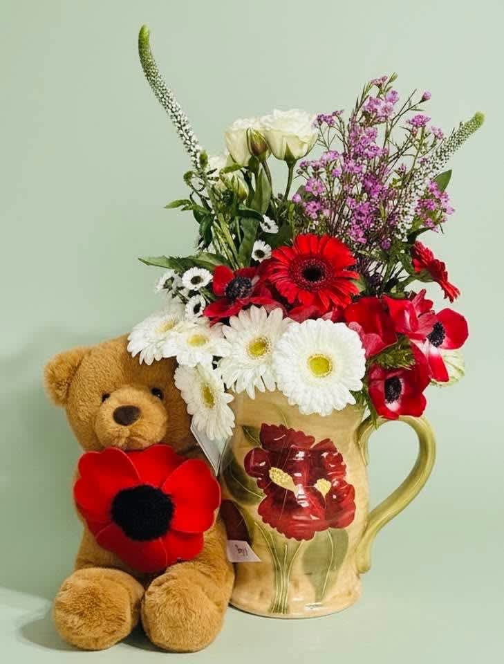 Bouquet in a floral mug beside a teddy bear with red flower accents