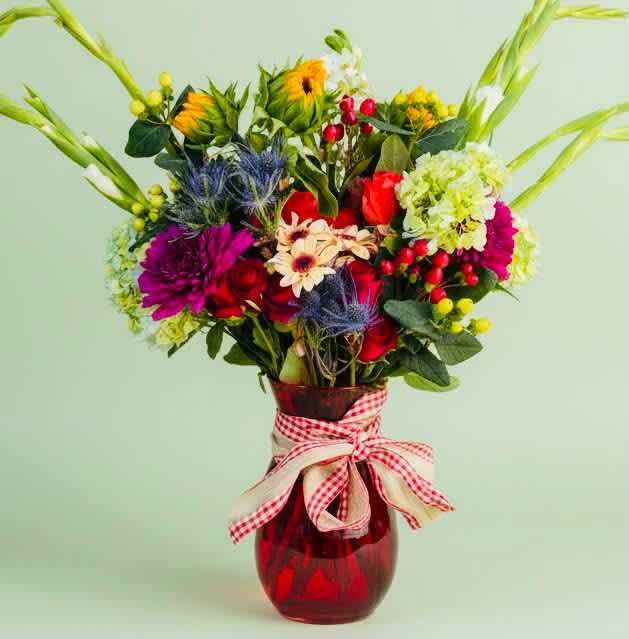 Colorful mixed bouquet in a red glass vase with a gingham ribbon
