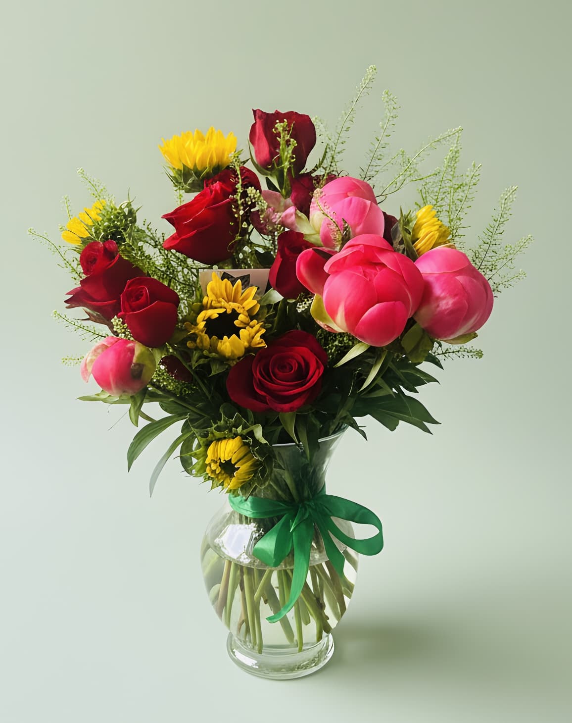 Mixed bouquet of red roses, pink peonies, and yellow sunflowers in a glass vase