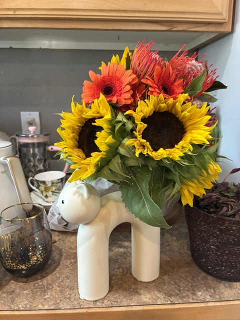 Bright sunflower bouquet with orange gerbera daisies in a white dog-shaped vase