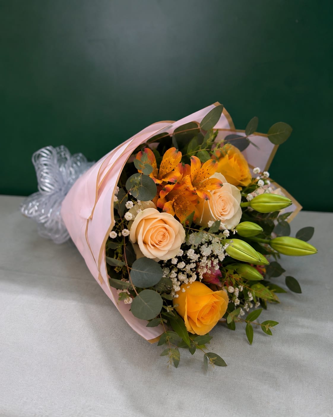 Bouquet of peach and yellow roses with orange lilies wrapped in pink paper