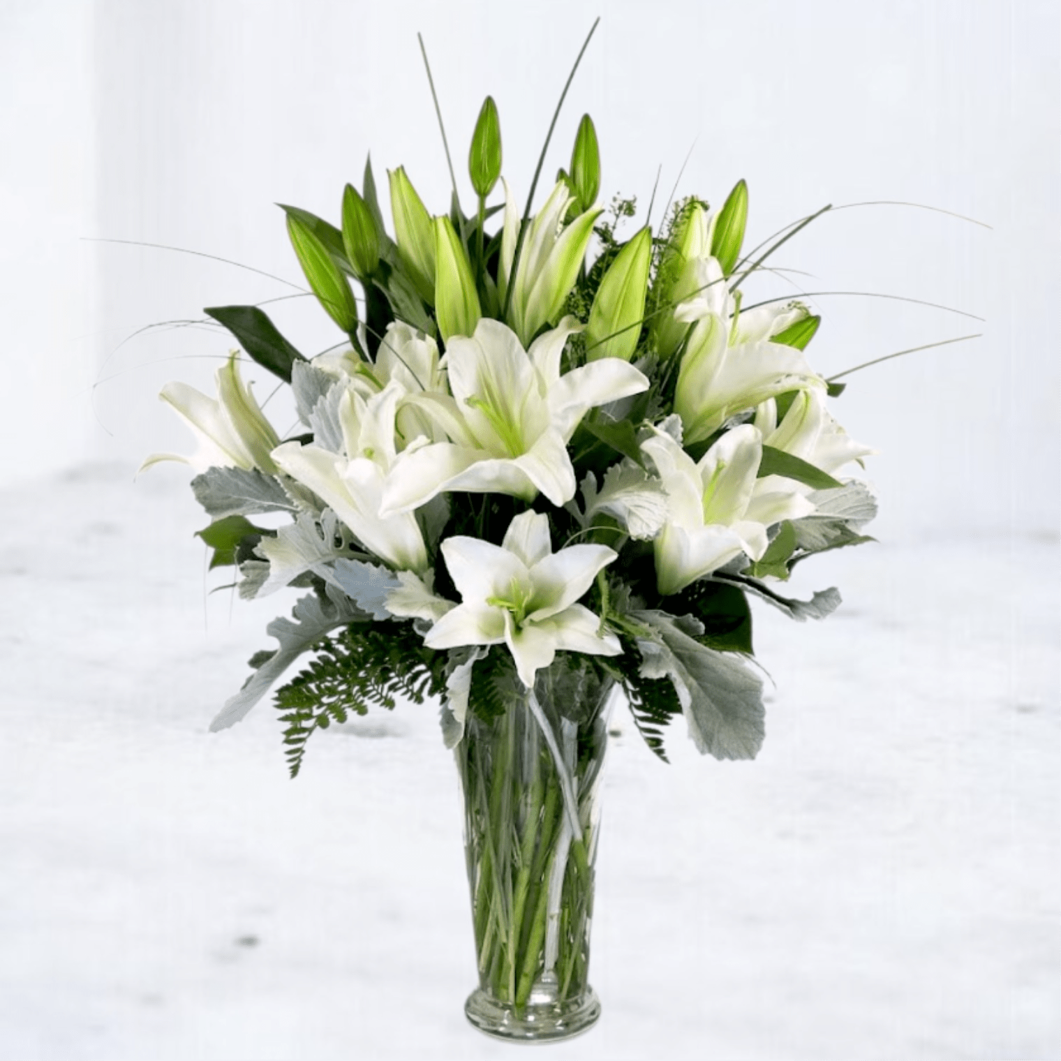 White lilies arranged in a clear glass vase with silver foliage