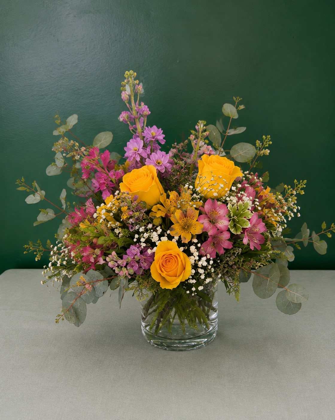 Mixed bouquet of yellow roses and pink flowers in a glass vase