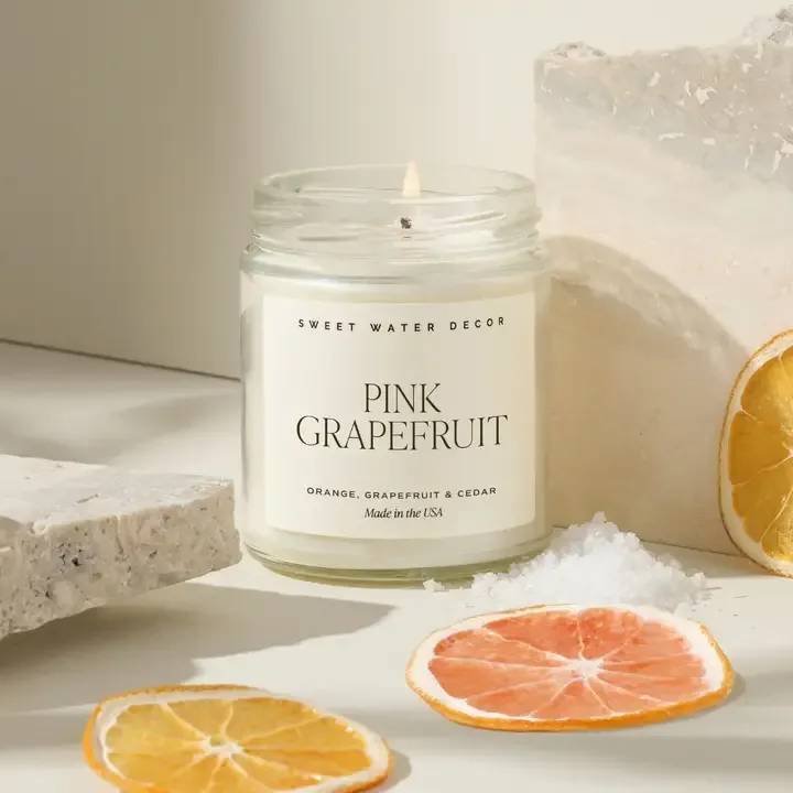 A lit pink grapefruit candle in a glass jar with dried citrus slices nearby.