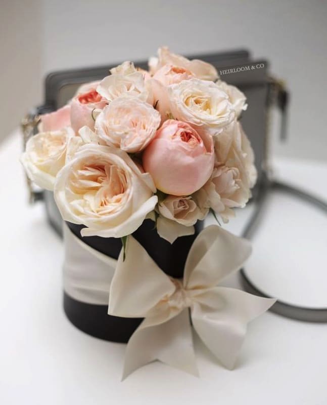 The Holly Go Lightly - Charming, playful, and bright, this arrangement was inspired by the very gracious Audrey Hepburn. The idea behind this piece was rather simple... to make someone smile, blush, and have a happy day. As Hepburn once said "Happy girls are the prettiest."  This piece consists of two premium garden rose favorites; The Juliette, and the White O'Hara. We also sprinkle in a touch of mini roses with big full blooms to top off the perfectly rounded shape, and wrap it up with a bow we know Audrey would most certainly approve of.