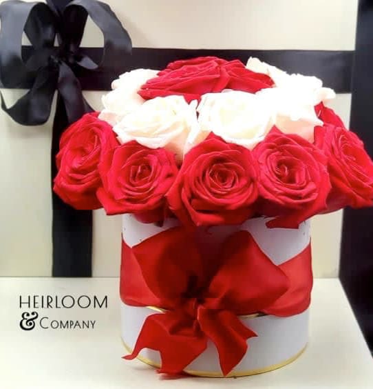 Red and white roses arranged in a round gift box with a black ribbon