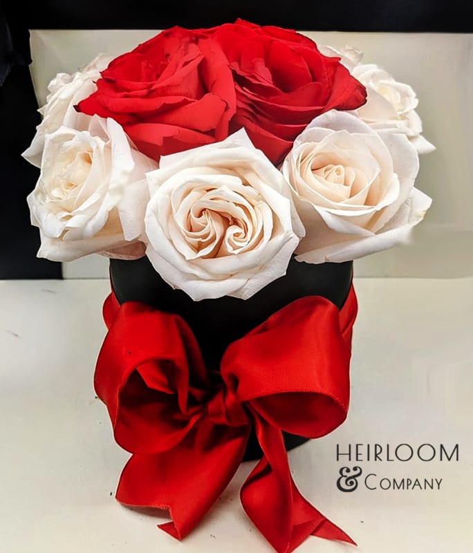 Red and white roses arranged in a black hat box with a red ribbon