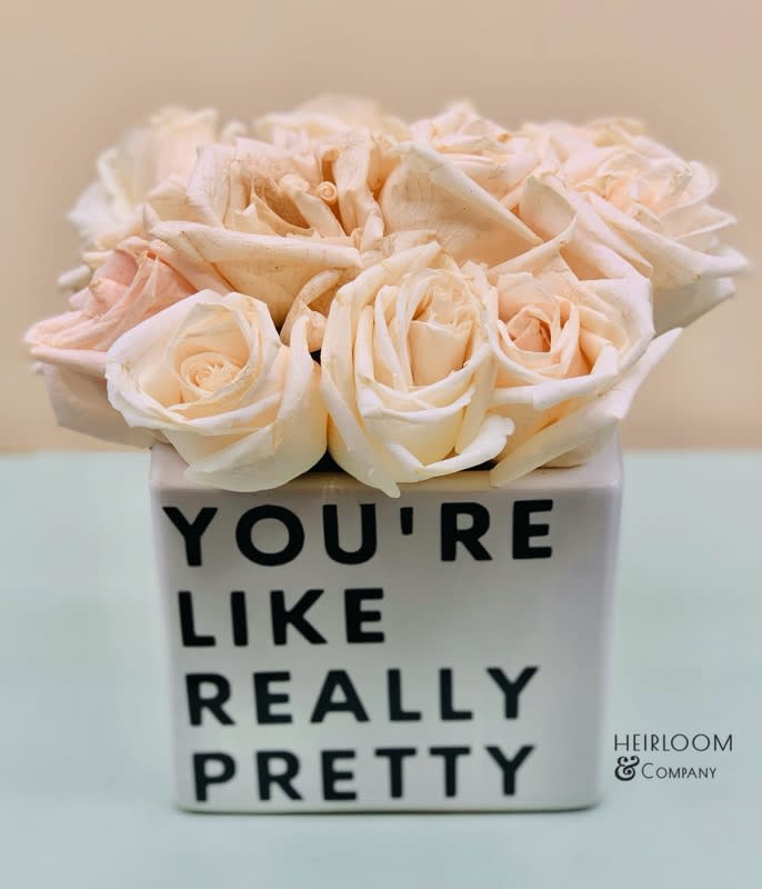 Cream roses in a white square vase with black text