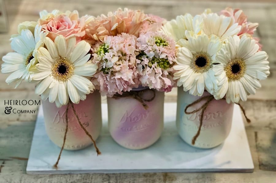 Three pastel mason jars with daisy and pink flower arrangements