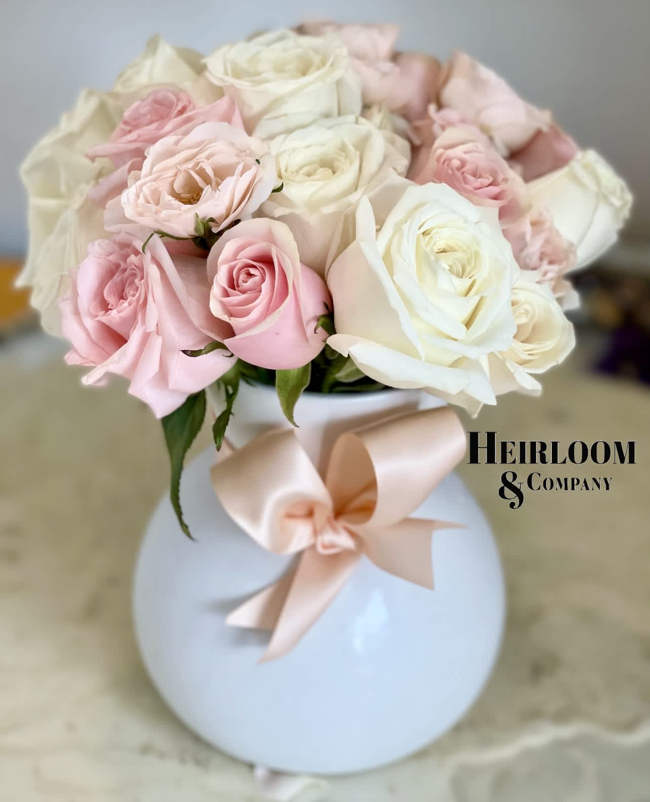 Pink and white roses in a round white vase with a blush ribbon