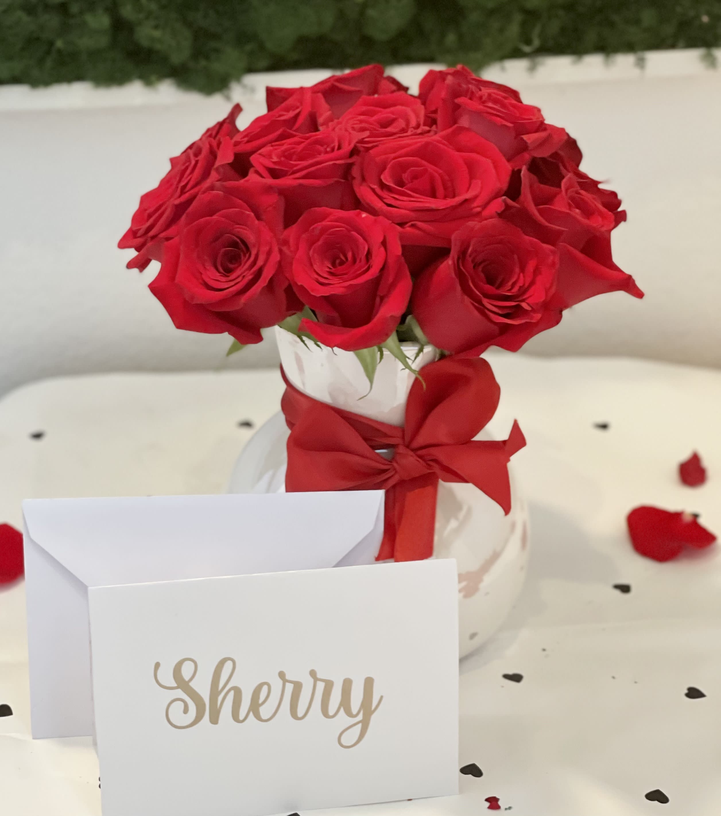 Red roses in a white vase with a red ribbon and a name card