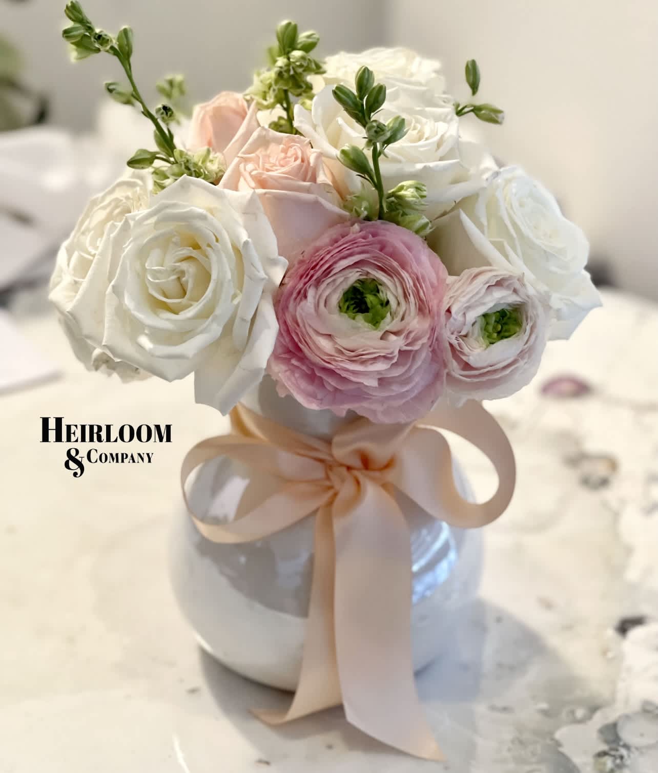 Pink and white roses with ranunculus in a white vase tied with a blush ribbon