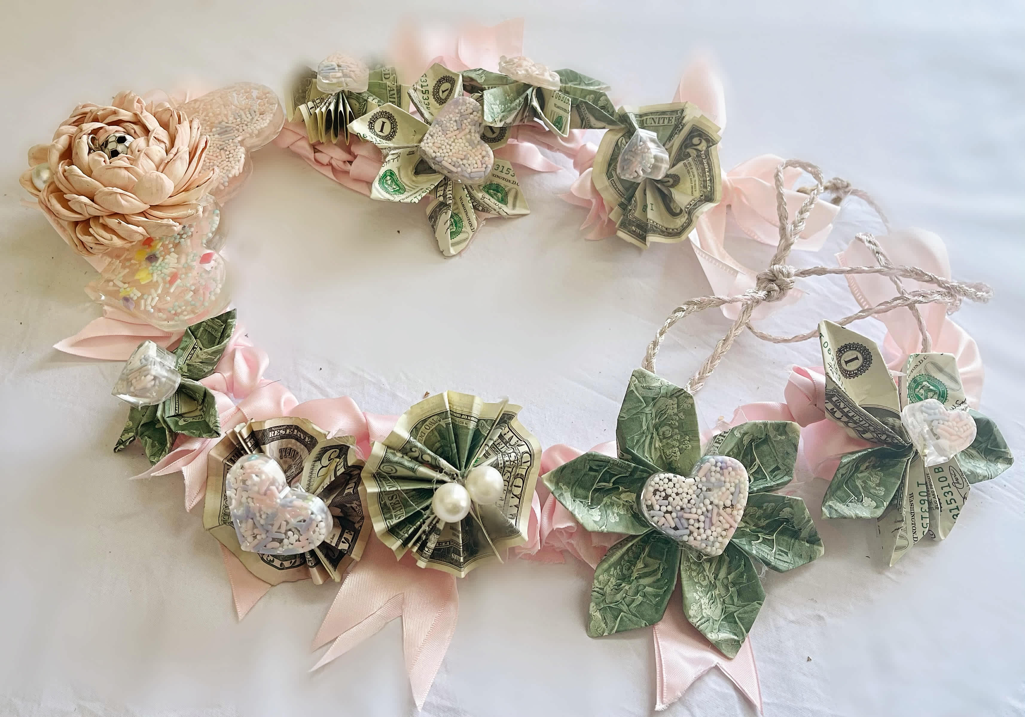 Money lei with pink ribbon and paper flowers on a white surface