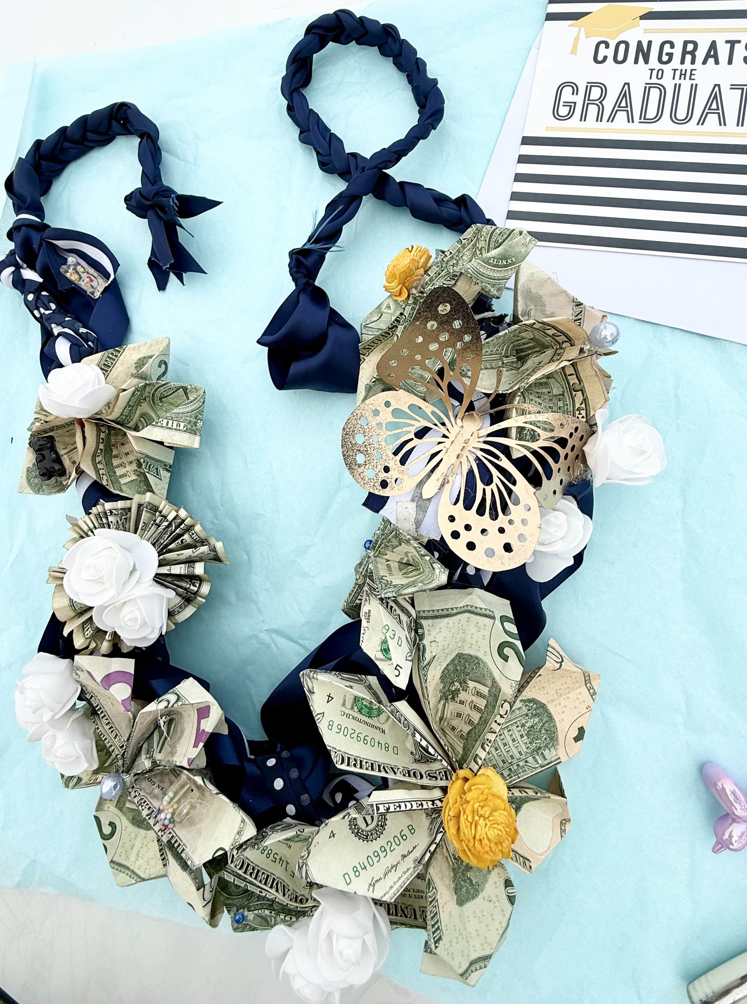 Money lei with ribbon and paper flowers beside a graduation card