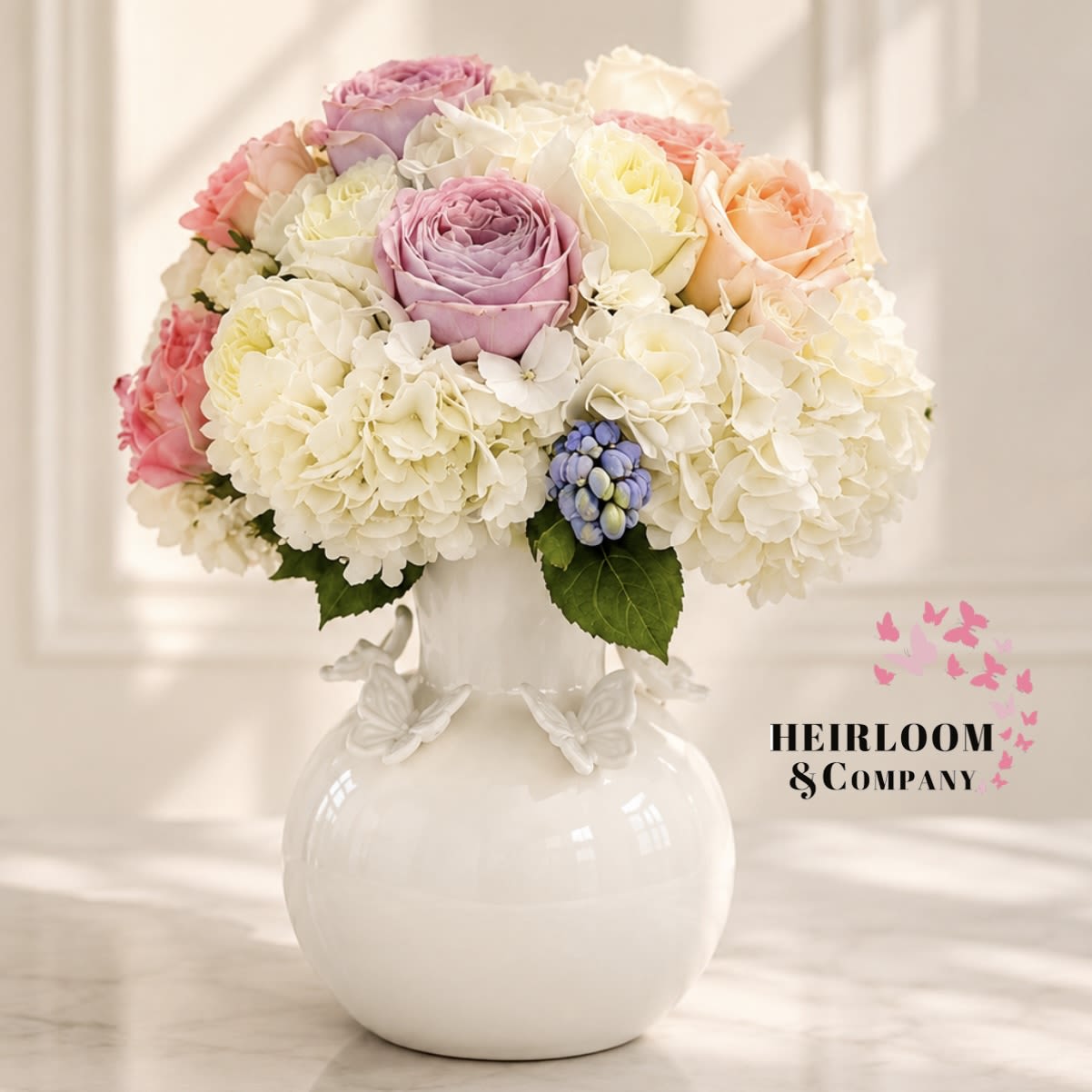Butterflies and Bouquets  - An abundant luxury arrangement featuring blush roses, premium garden roses, white hydrangea, and soft pastel textures arranged in a whimsical ceramic butterfly vase. Romantic and airy, this design is inspired by elegant English garden florals with a moder