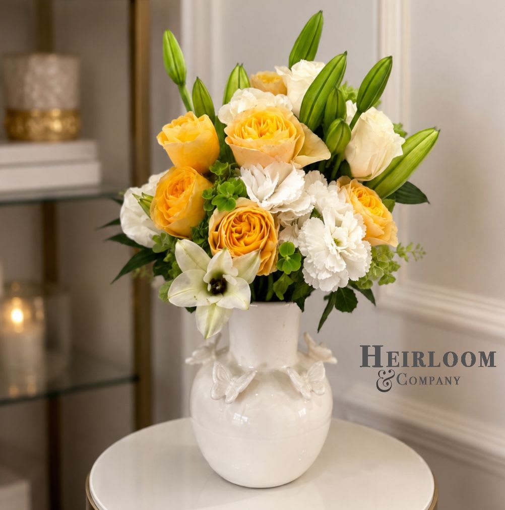 Summer - Premium yellow garden roses, white lilies, and textured seasonal blooms are gathered in our signature butterfly vase for a design that feels both fresh and timeless.  The combination of soft ivory and golden tones creates a sophisticated arrangement suitable for birthdays, celebrations, thank-you gifts, and everyday moments worth recognizing.  Hand-designed by Heirloom &amp; Company using the freshest blooms available. Flower varieties may vary slightly based on seasonal availability.