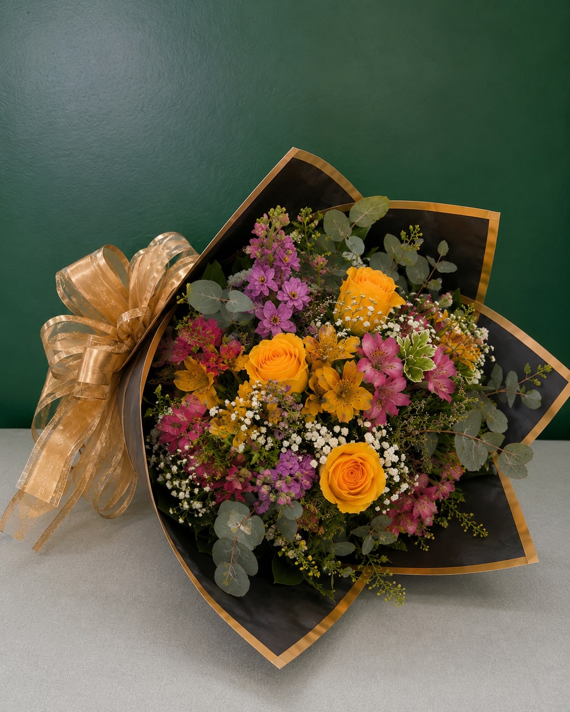 Bouquet of yellow roses and pink-purple mixed flowers wrapped in black paper with gold trim