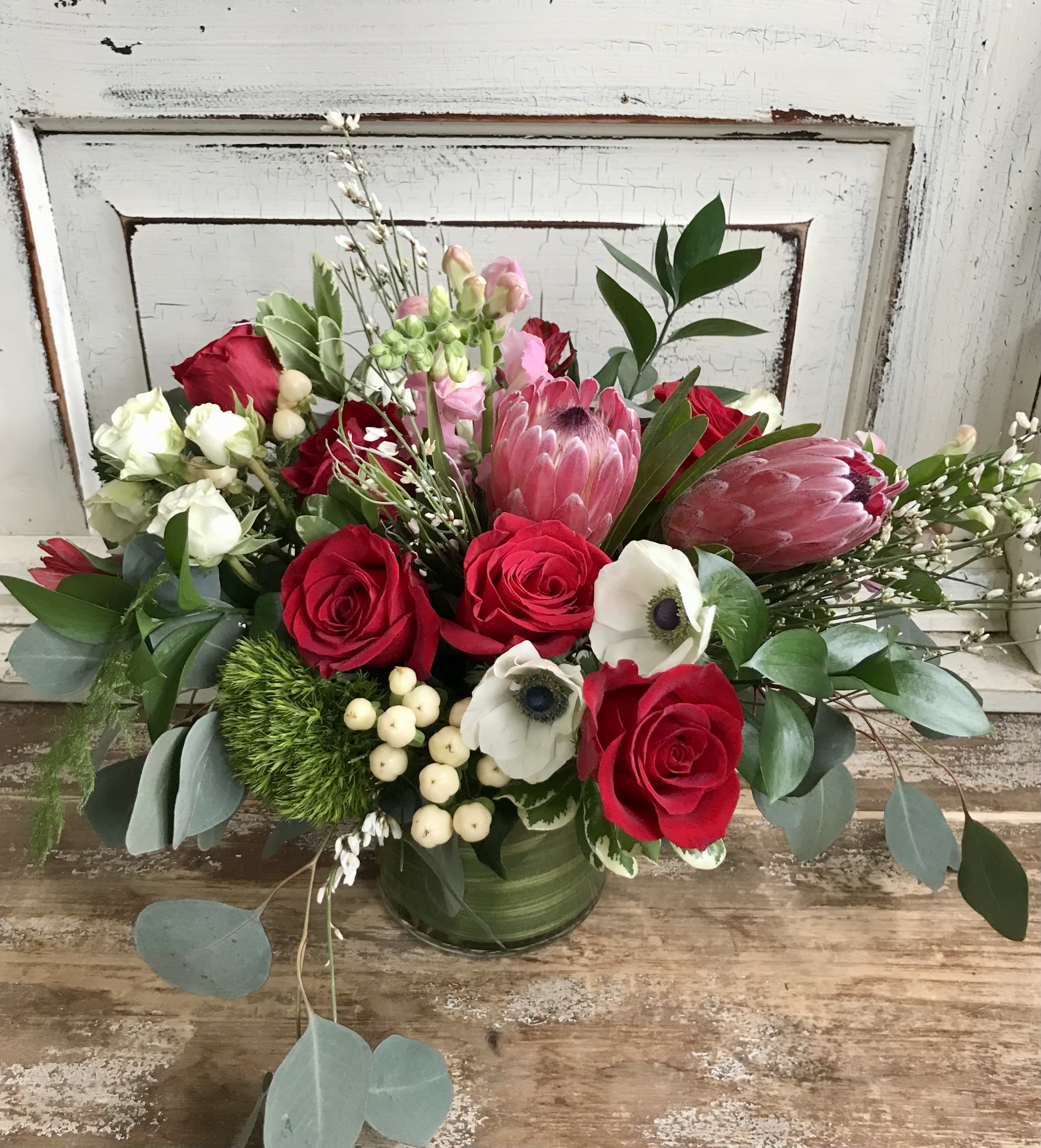 Bouquet of red roses and pink protea in a green vase