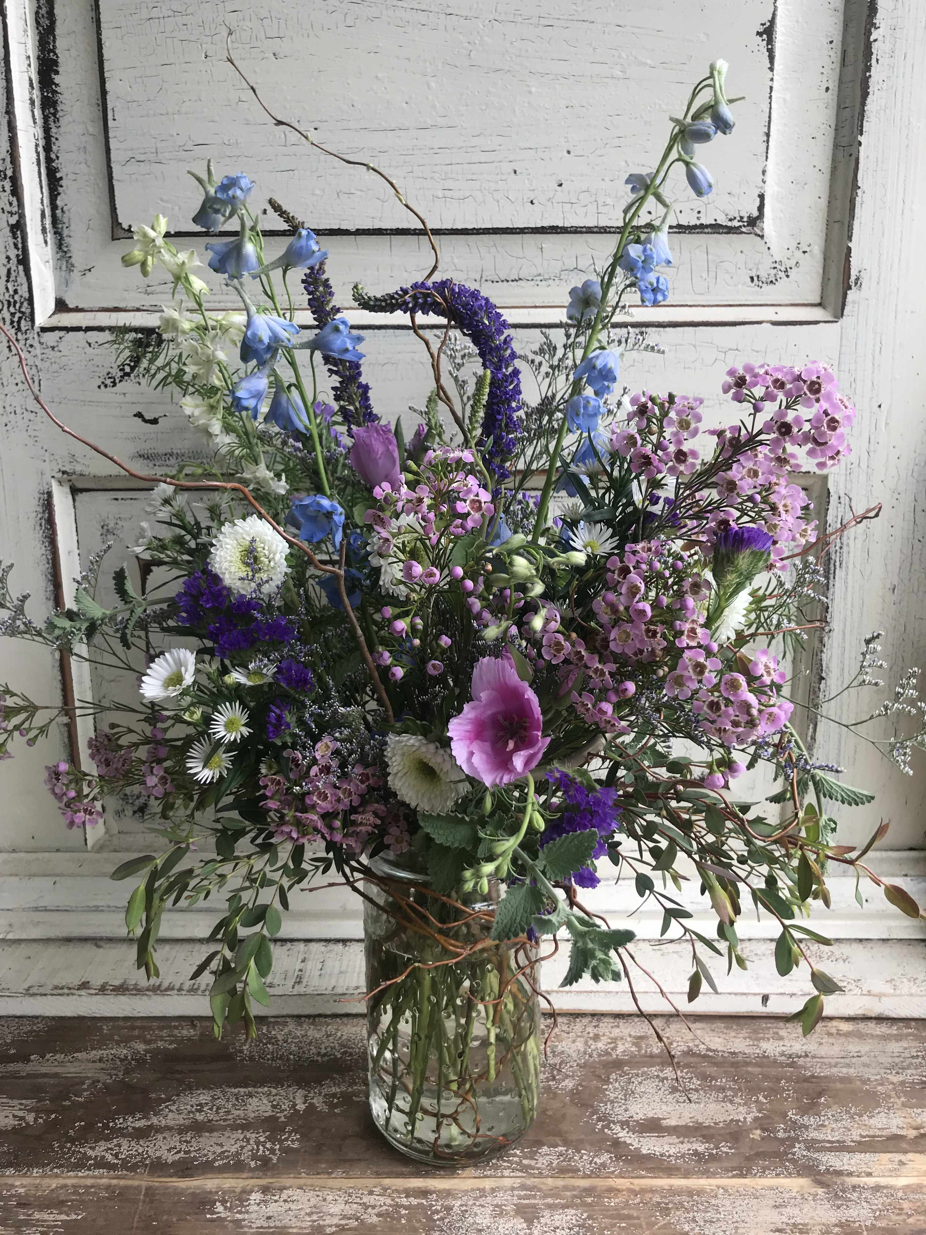 Mixed bouquet of blue, pink, and white flowers in a clear glass vase