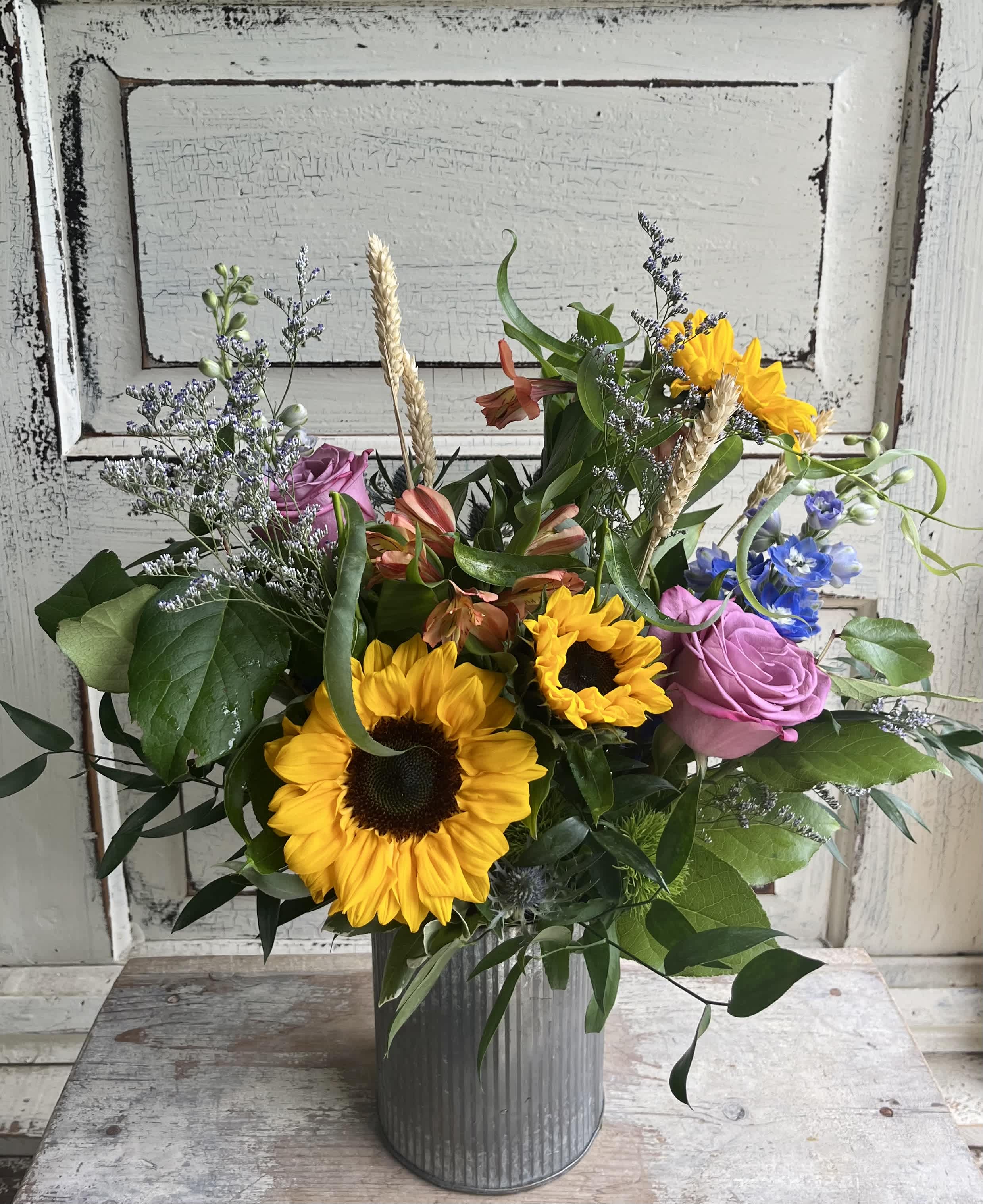 Mixed bouquet with sunflowers, pink roses, and blue flowers in a metal vase