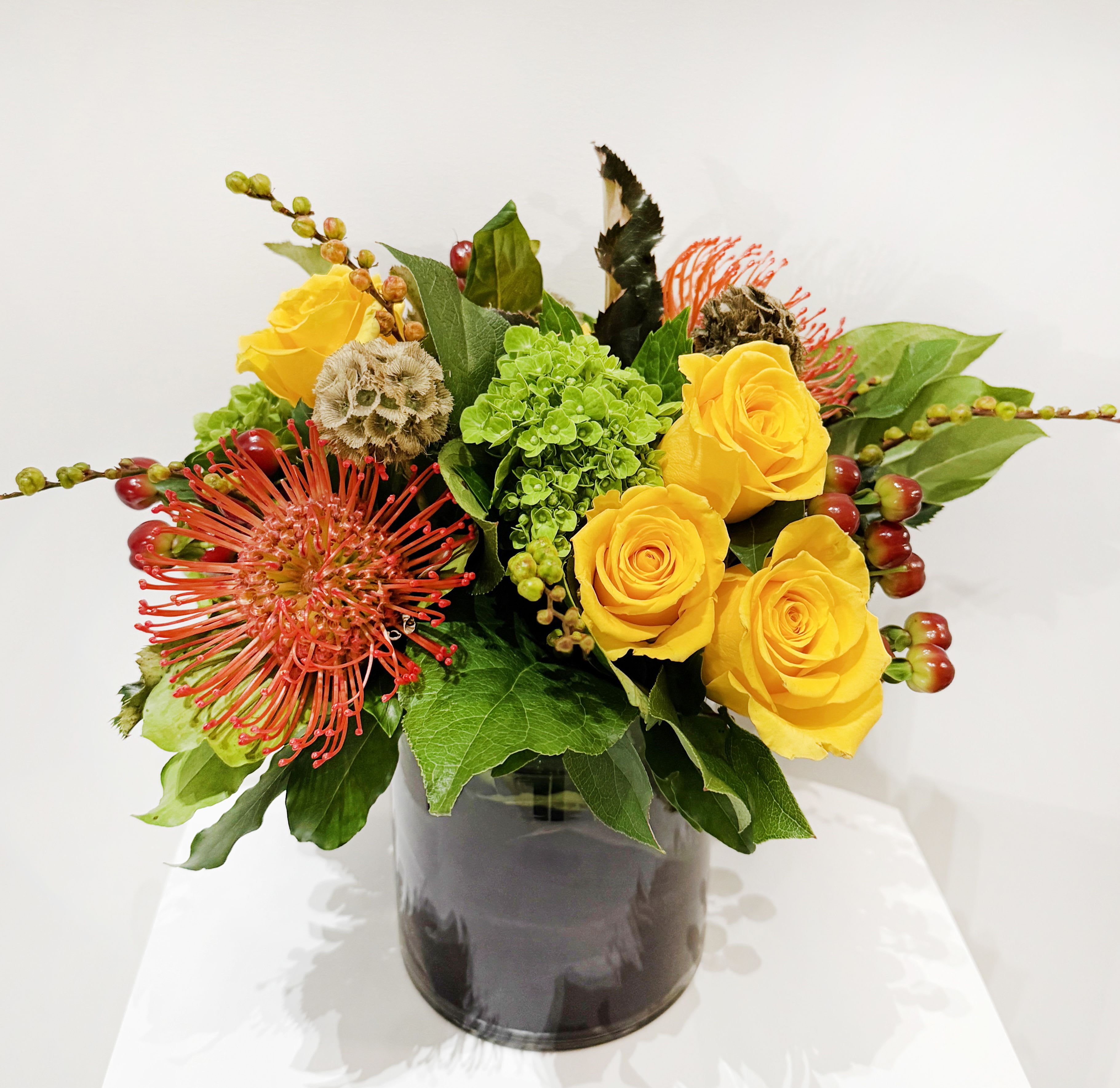 Yellow roses and red pincushion blooms in a dark vase