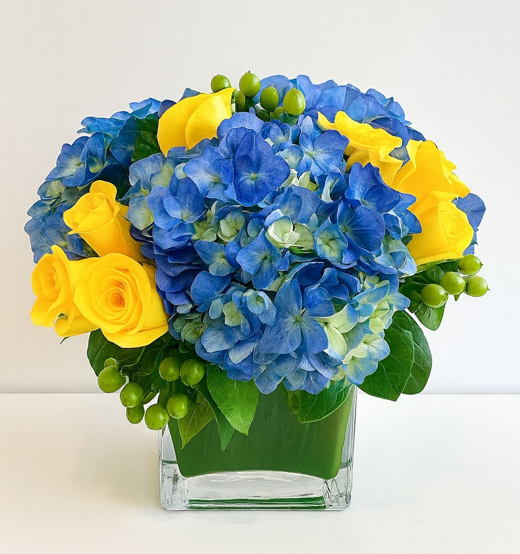 Blue hydrangeas and yellow roses in a clear square vase