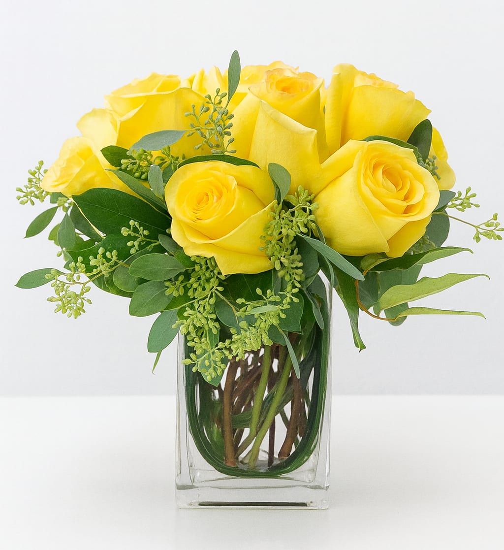 Yellow roses arranged in a clear glass vase with greenery