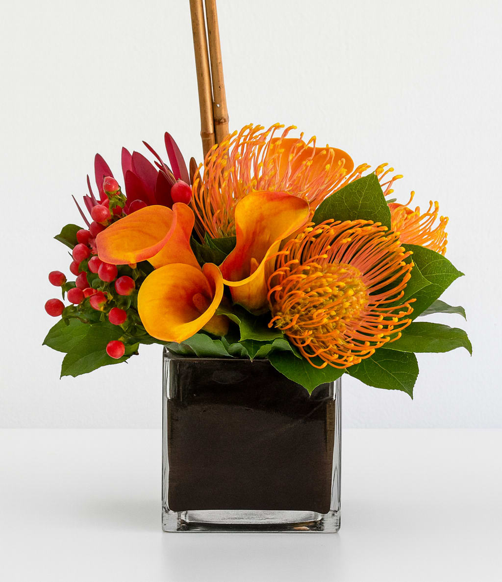Orange calla lilies and pincushion protea in a square glass vase