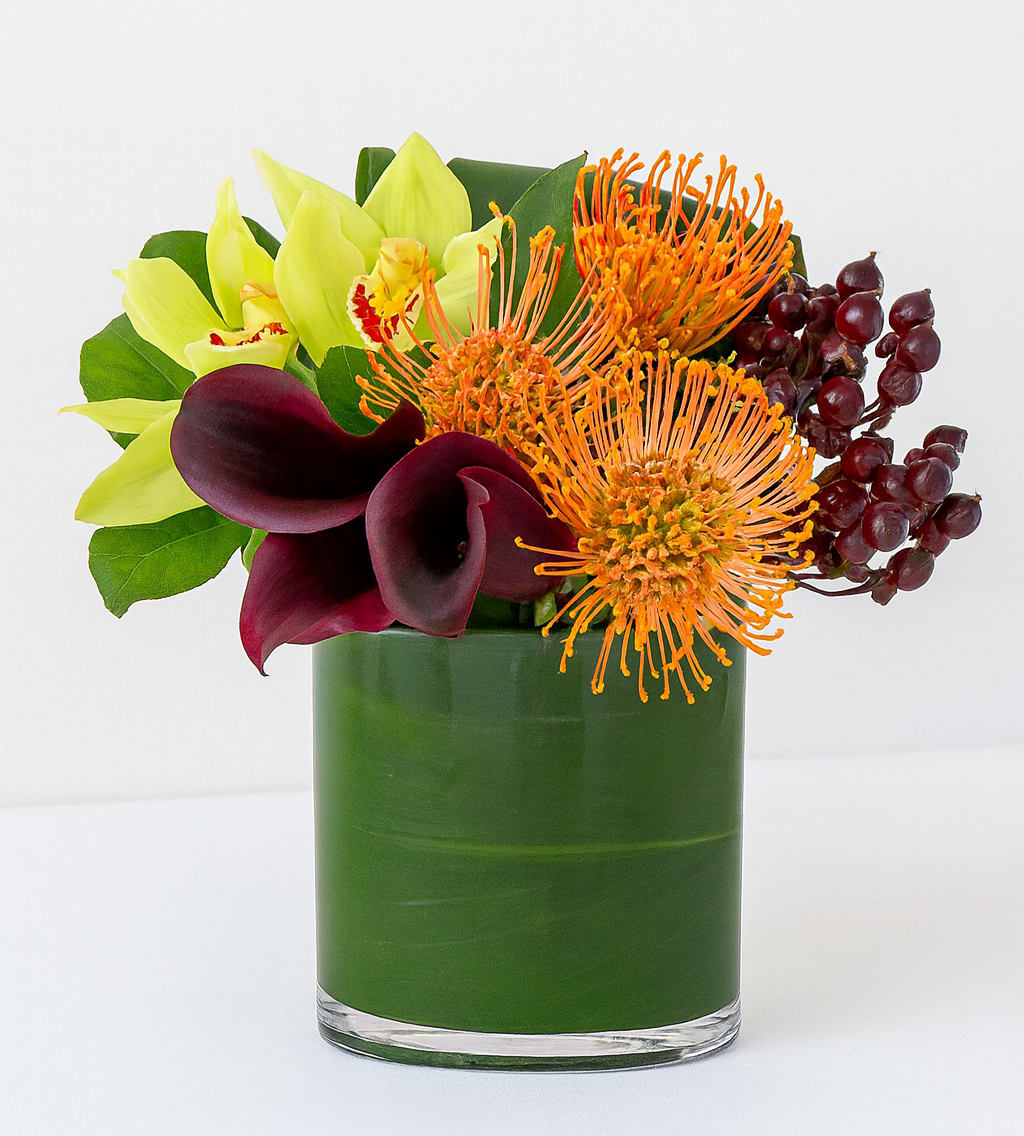 Bouquet of yellow orchids, orange pincushion blooms, and burgundy calla lilies in a green vase