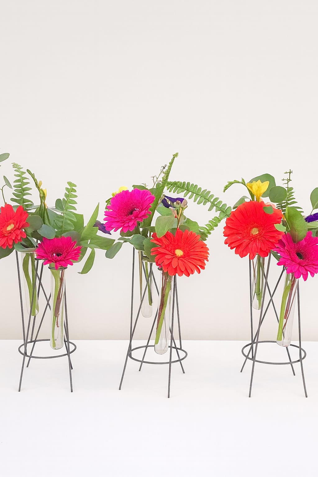 Bright gerbera daisies in slim glass vases on metal stands