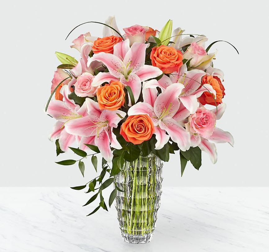 Pink lilies and orange roses arranged in a clear glass vase
