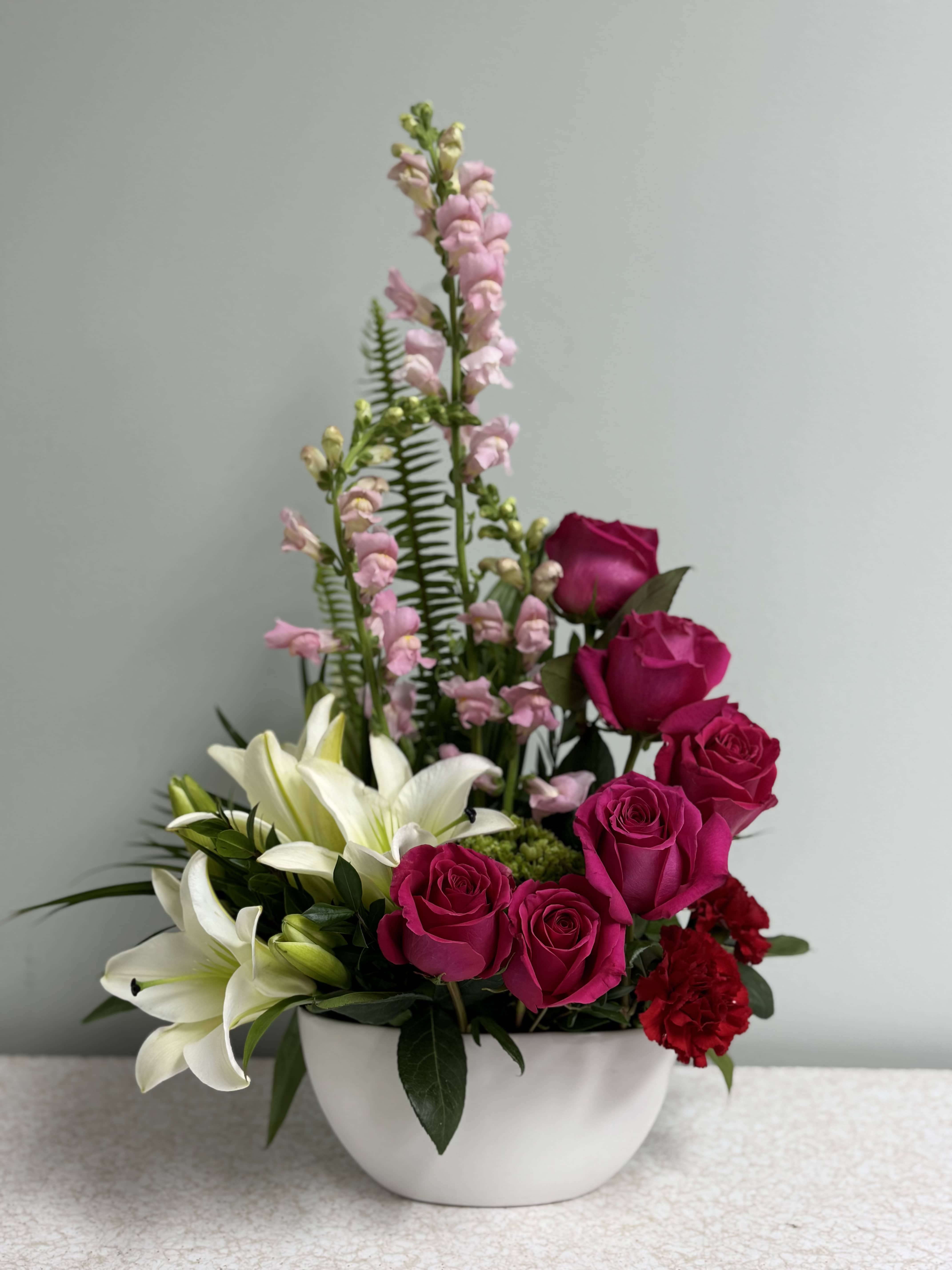 Pink roses and white lilies arranged in a white bowl vase