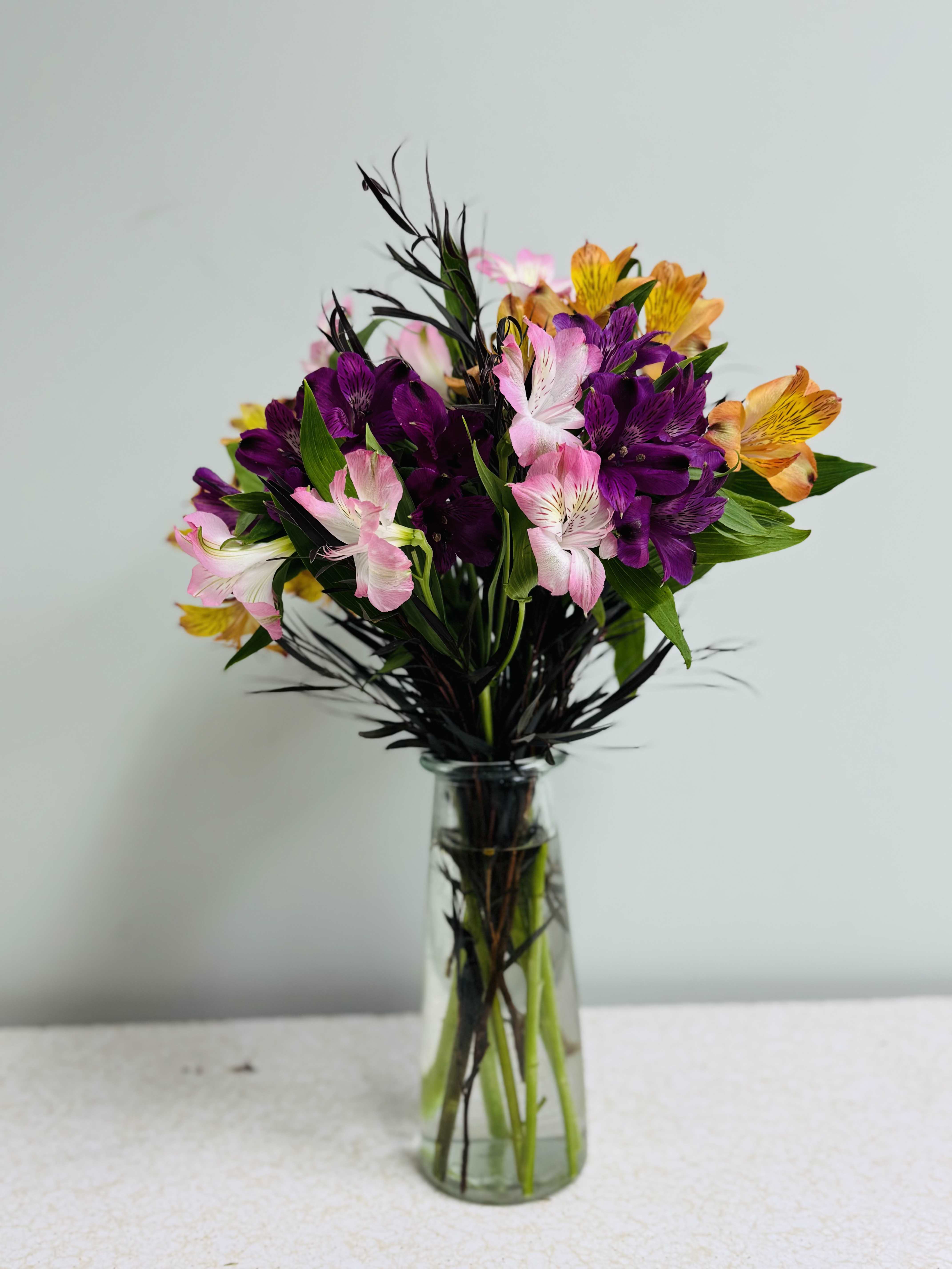 Bouquet of purple, pink, and orange flowers in a clear glass vase