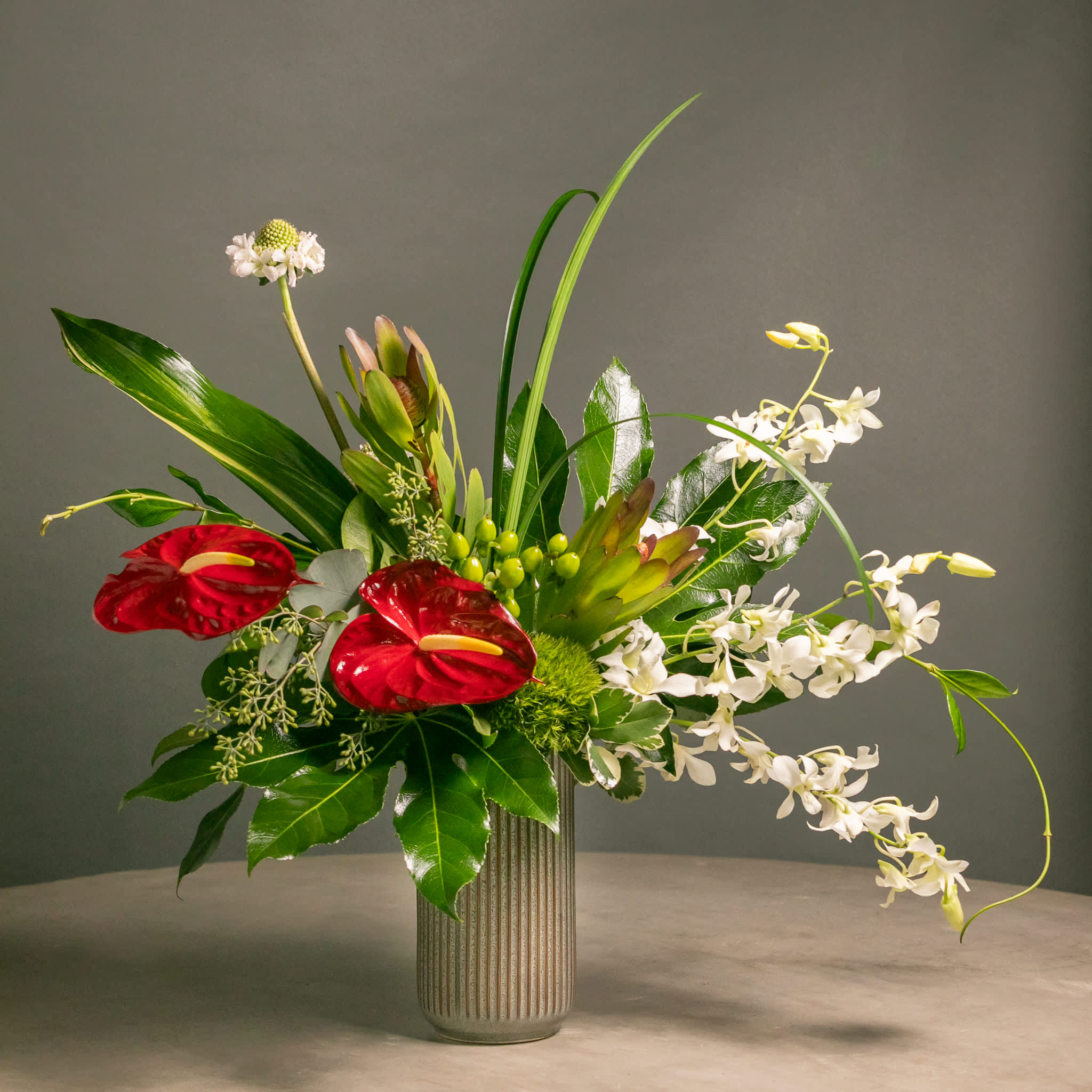 Tropical floral arrangement with red anthuriums and white orchids in a ribbed vase