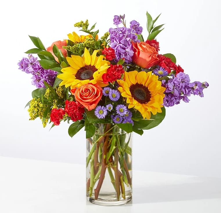 Mixed bouquet with sunflowers, roses, and purple flowers in a glass vase