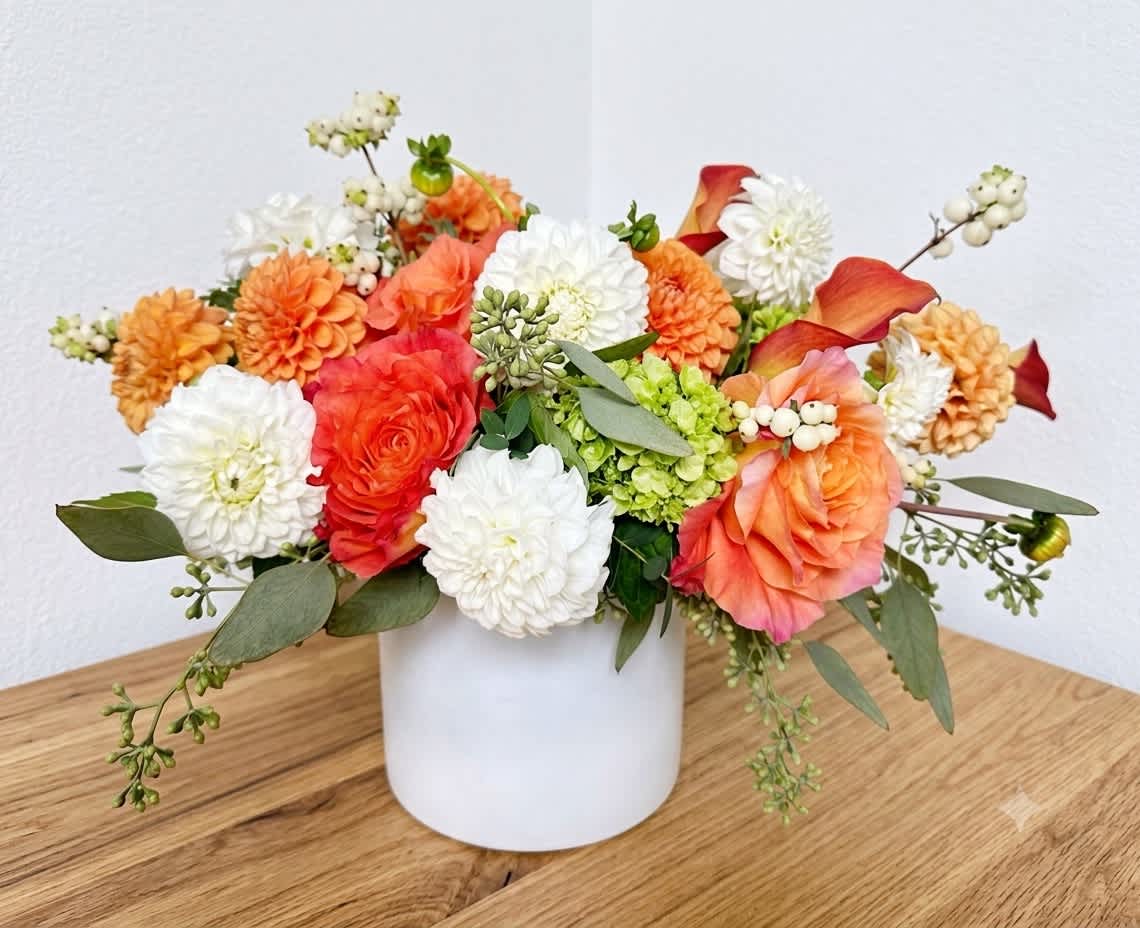 Mixed orange, white, and coral flowers arranged in a white vase