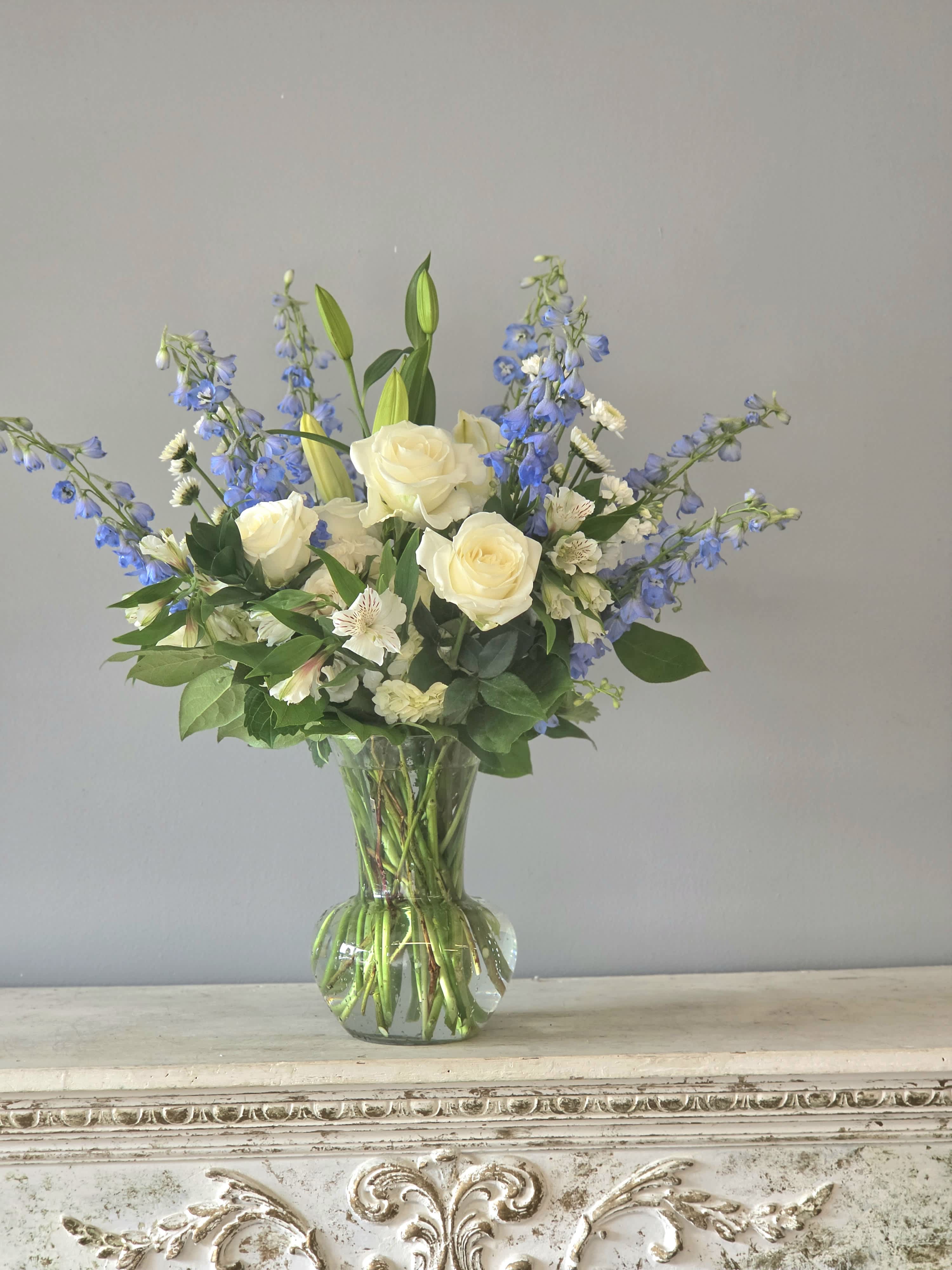 White roses and blue delphinium in a clear glass vase