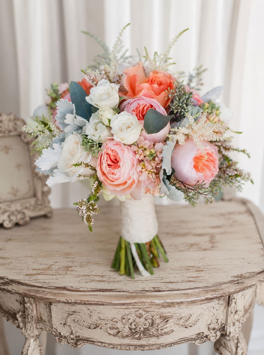 Romance bouquet - A rounded cluster of peach, blush pink, and white roses creates an instantly romantic wedding bouquet designed to make the person you're thinking of feel cherished. This bridal-style bouquet reads soft and garden-fresh-perfect for a wedding, anniversary, or any romantic celebration where you want her to feel truly seen.  Tightly packed roses are layered with airy filler and muted blue-green foliage for a textured, soft silhouette that photographs beautifully. The stems are hand-tied with a white wrapped handle and finished with a white ribbon, giving a refined, comfortable grip for carrying down the aisle. The pastel palette of pink, peach, white, and green lends a timeless, elegant look that complements lace, chiffon, or modern minimal gowns.  Ideal for brides, bridesmaids, or as an anniversary surprise, this bouquet sends a quiet, heartfelt message of love and tenderness. Order with standard sizing for a classic hand-held look; for any special requests about bloom count or delivery timing, include those details at checkout so the bouquet arrives ready to create the moment you intend.   If any design elements are of major importance to your order, please include them in the florist instructions at checkout or contact us to ensure availability.