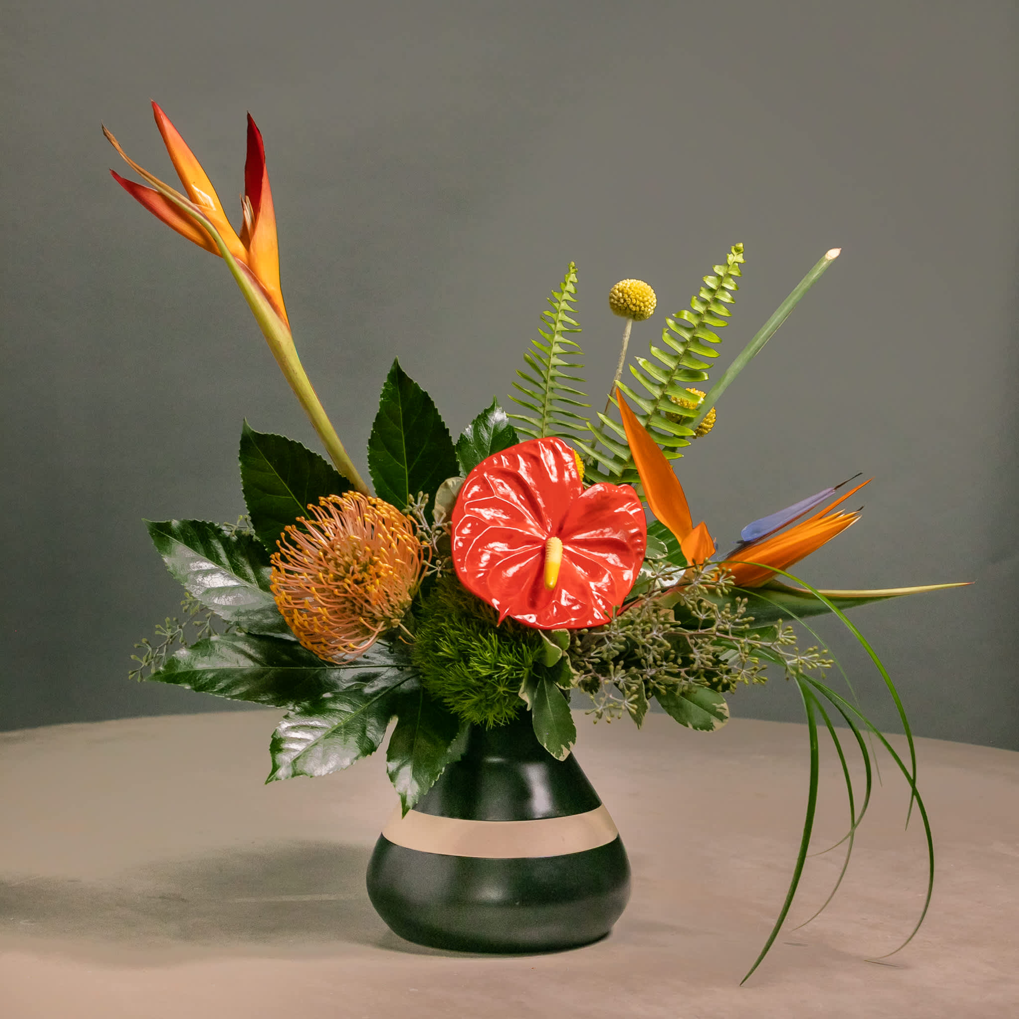 Tropical floral arrangement in a dark vase with orange and red blooms